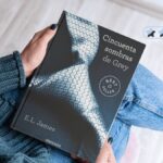 Resumen de Cincuenta sombras de Grey: una mujer sostiene el libro de E. L. James junto a una valoración de dos estrellas y media